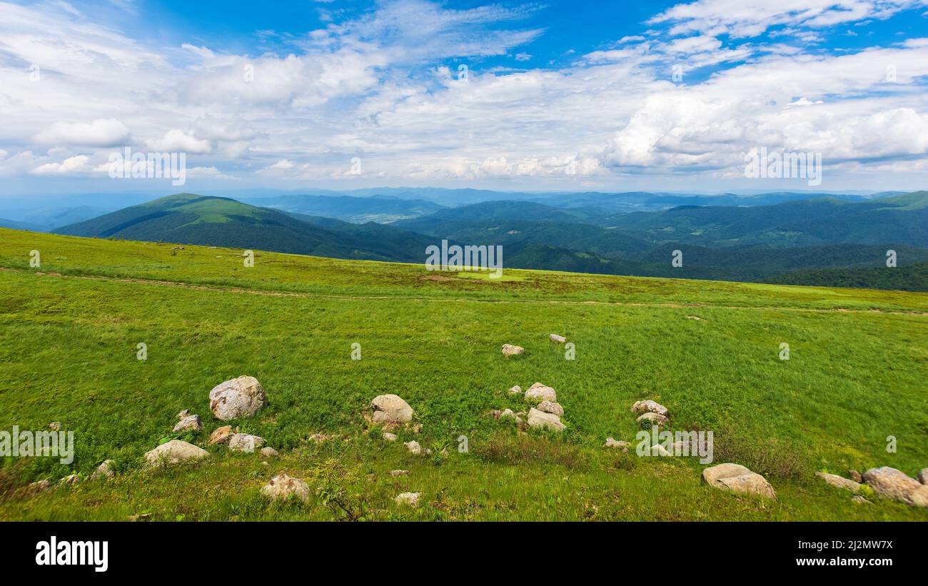 Grüne Sommerlandschaft in den Bergen. Außenlandschaft mit blauem Himmel und Wolken. Schöne Natur an einem sonnigen Tag. Steine auf dem grasbewachsenen Hügel Stockfoto