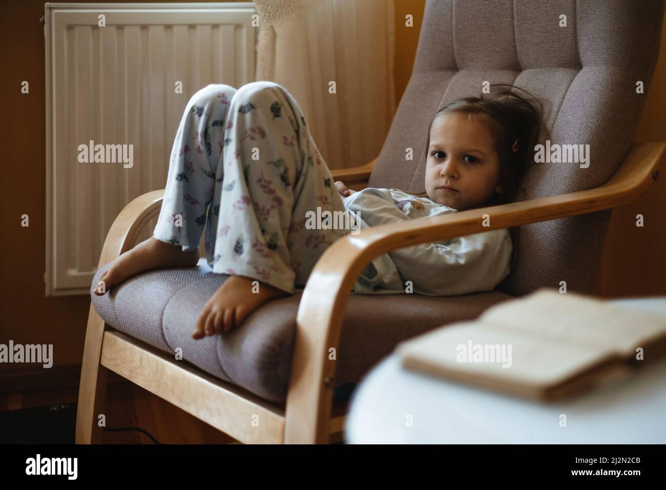 Gelangweilt traurig Kleinkind Kind einsam zu Hause sitzen auf Sessel. Trauriger, entspannter, ehrlicher Junge zu Hause in gemütlicher, warmer Atmosphäre. Mädchen denken, träumen. Kopieren Stockfoto