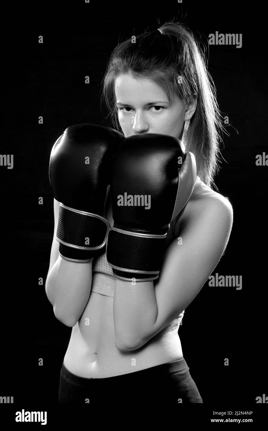 Hübsche Muay Thai Boxerin in Angriffsstellung. Fitness junge Frau Boxtraining auf schwarzem Hintergrund, Nahaufnahme einfarbig Stockfoto