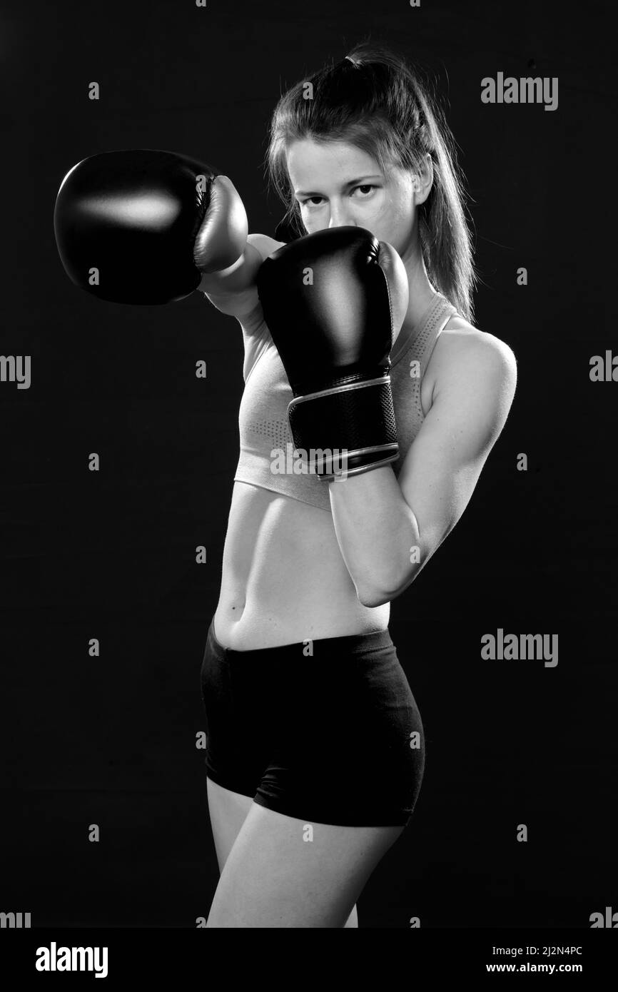 Hübsche Muay Thai Boxerin in Angriffsstellung. Fitness junge Frau Boxtraining auf schwarzem Hintergrund, Nahaufnahme einfarbig Stockfoto