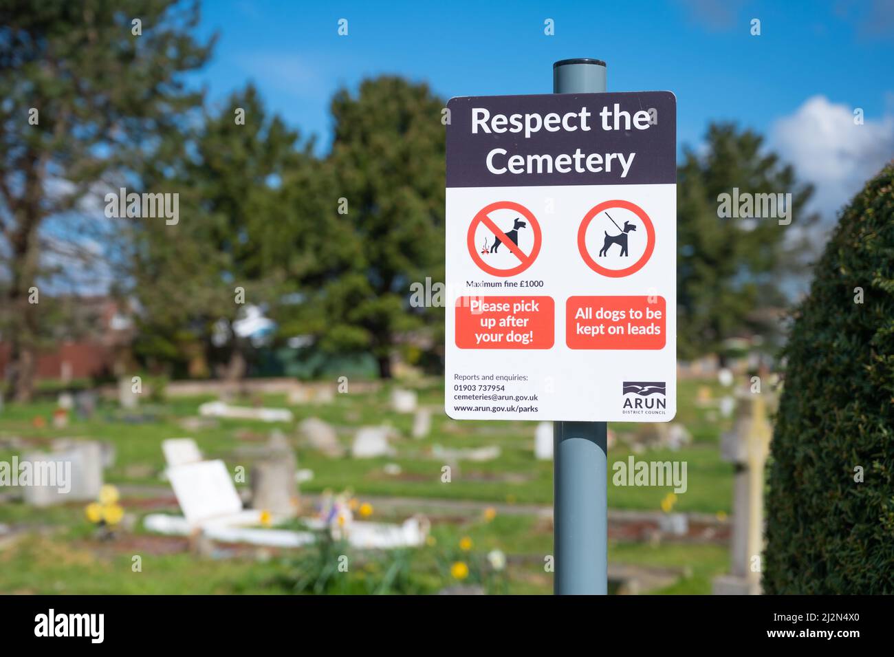 Schild auf einem Friedhof, der die Menschen auffordert, den Friedhof zu respektieren, indem sie Hunde an der Leine unter Kontrolle halten und ihren Poo in England abholen. Stockfoto