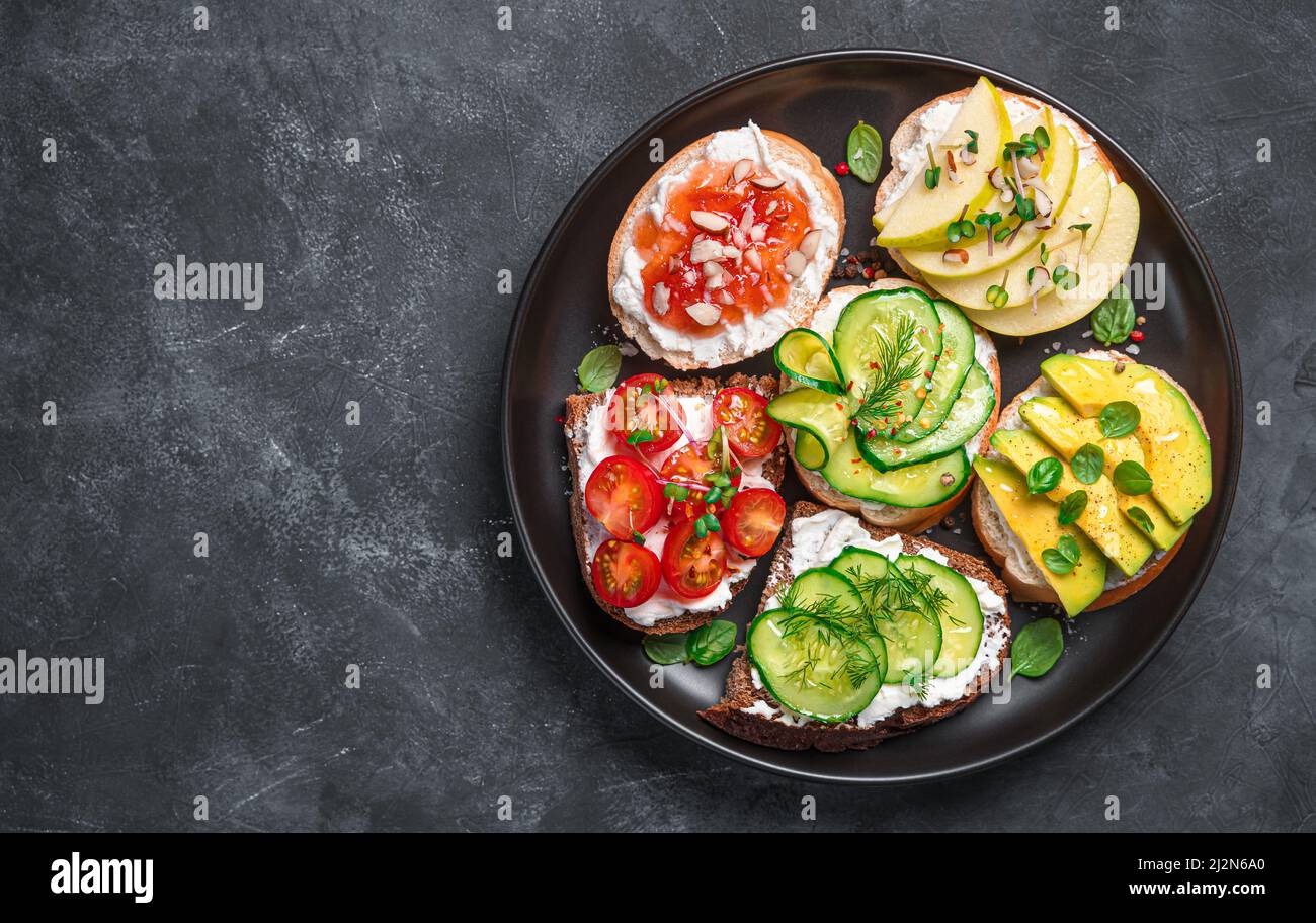 Verschiedene Sandwiches mit Weichkäse, Gemüse und Obst auf dunklem Hintergrund. Stockfoto