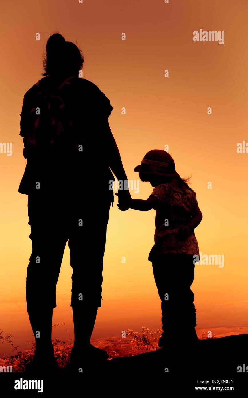 Silhouette Rückansicht von Mutter und Tochter, die sich bei Sonnenuntergang im Urlaub die Hand zusammenklatschen. Farbenfrohe Himmel Hintergrund orange und Gold Farben Sonnenuntergang Himmel. F Stockfoto
