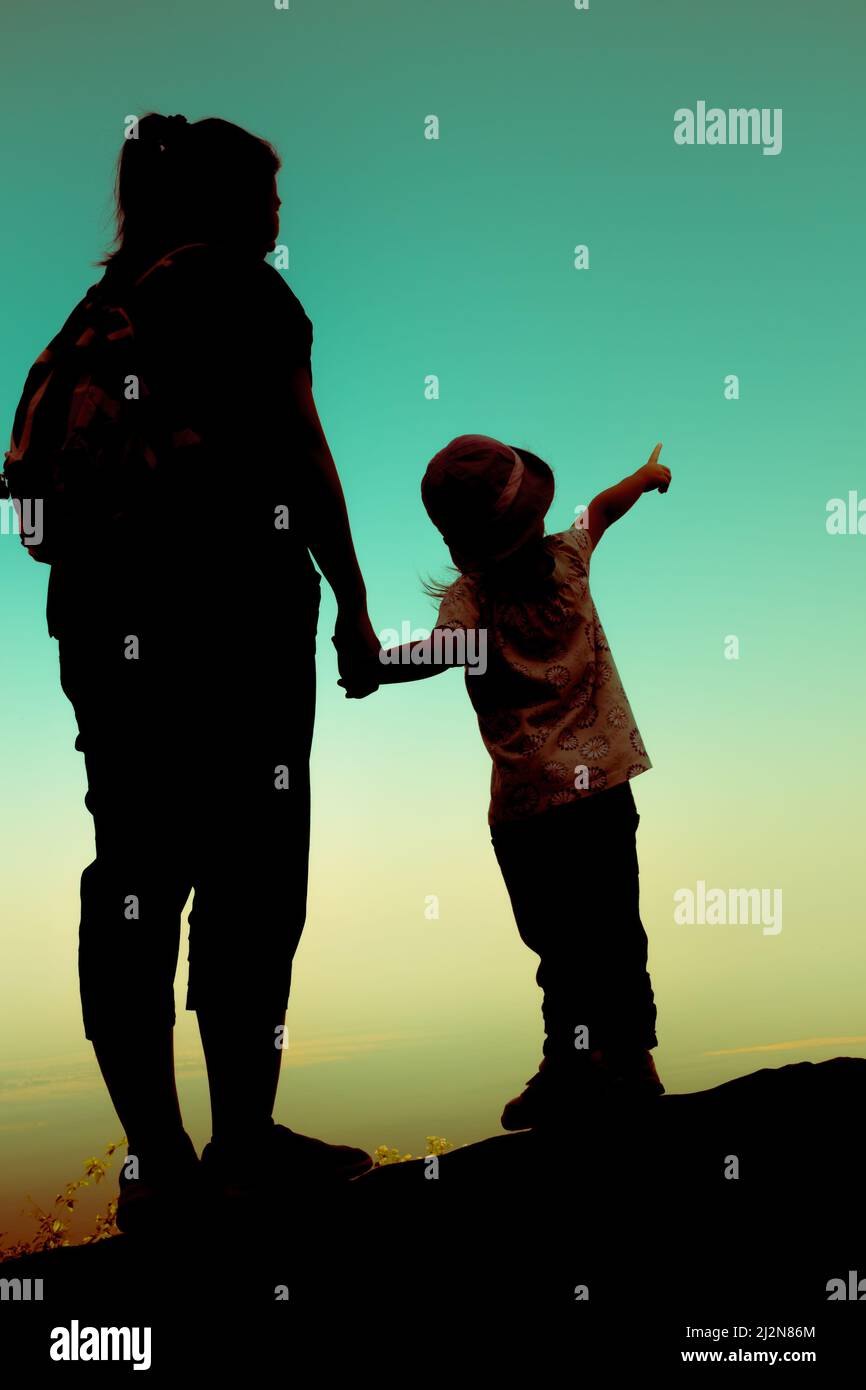 Silhouette Rückansicht von Mutter und Tochter zusammenklammend Hand. Mädchen zeigen zum Himmel. Freundliche Familie. Prozessübergreifend. Stockfoto