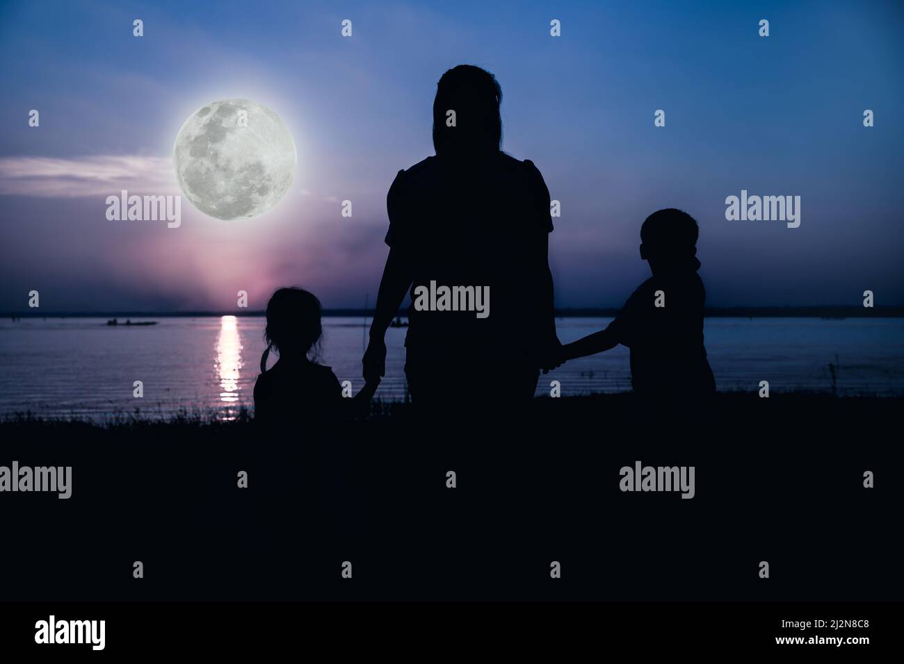 Silhouette von Eltern und Kindern, die die Aussicht am Flussufer genießen. Farbenfroher blauer Himmel und heller Vollmond-Hintergrund. Freundliche Familie. Kühle Farben Ton ph Stockfoto