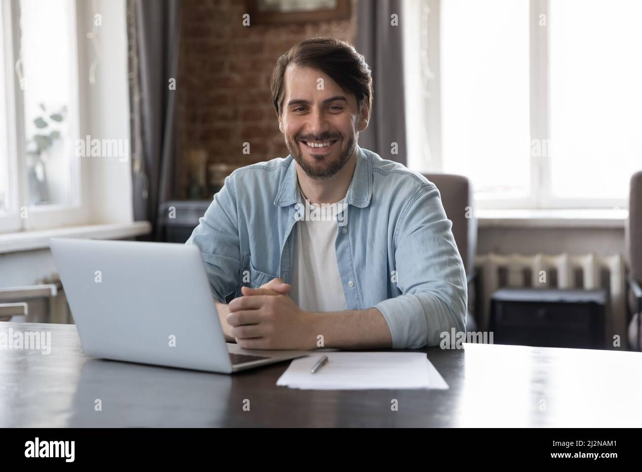 Glücklicher, selbstbewusster Projektleiter, der mit einem Laptop am Arbeitsplatz sitzt Stockfoto