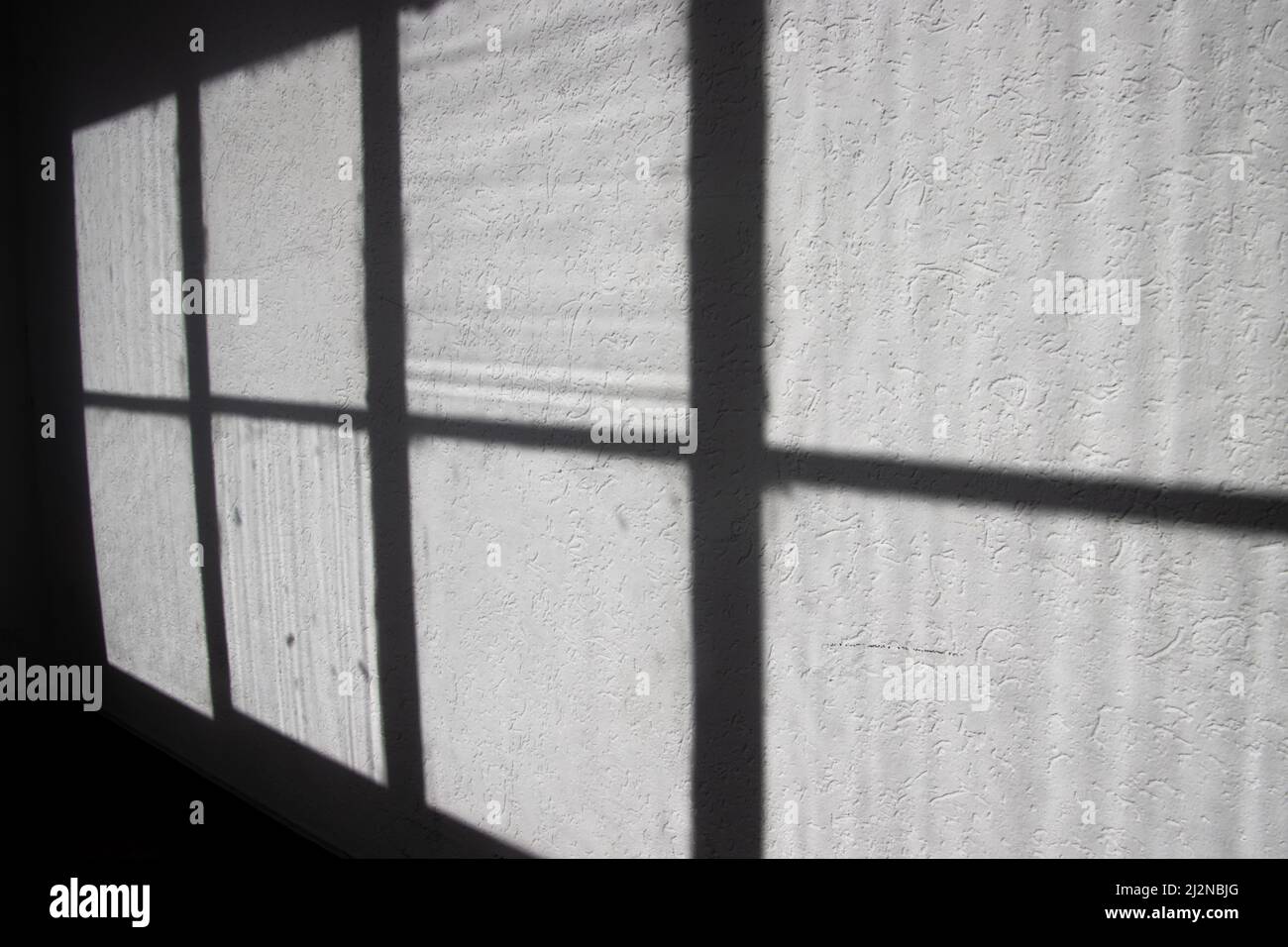 Licht und Schatten eines alten Fensterrahmens an einer weißen, grungigen Wand Stockfoto
