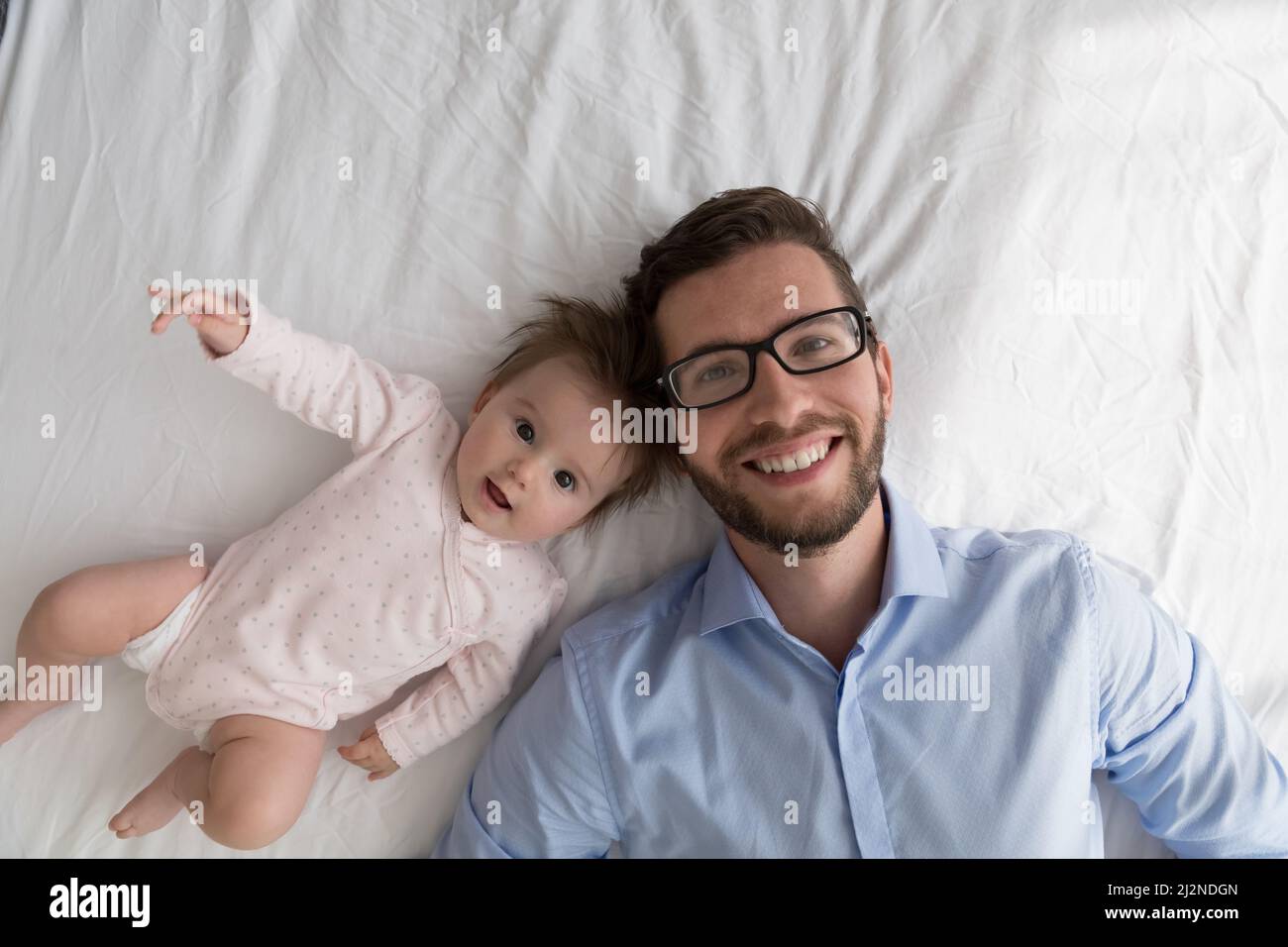 Fröhlicher Vater und entzückendes Baby ruhen sich zusammen auf einem großen Bett aus Stockfoto