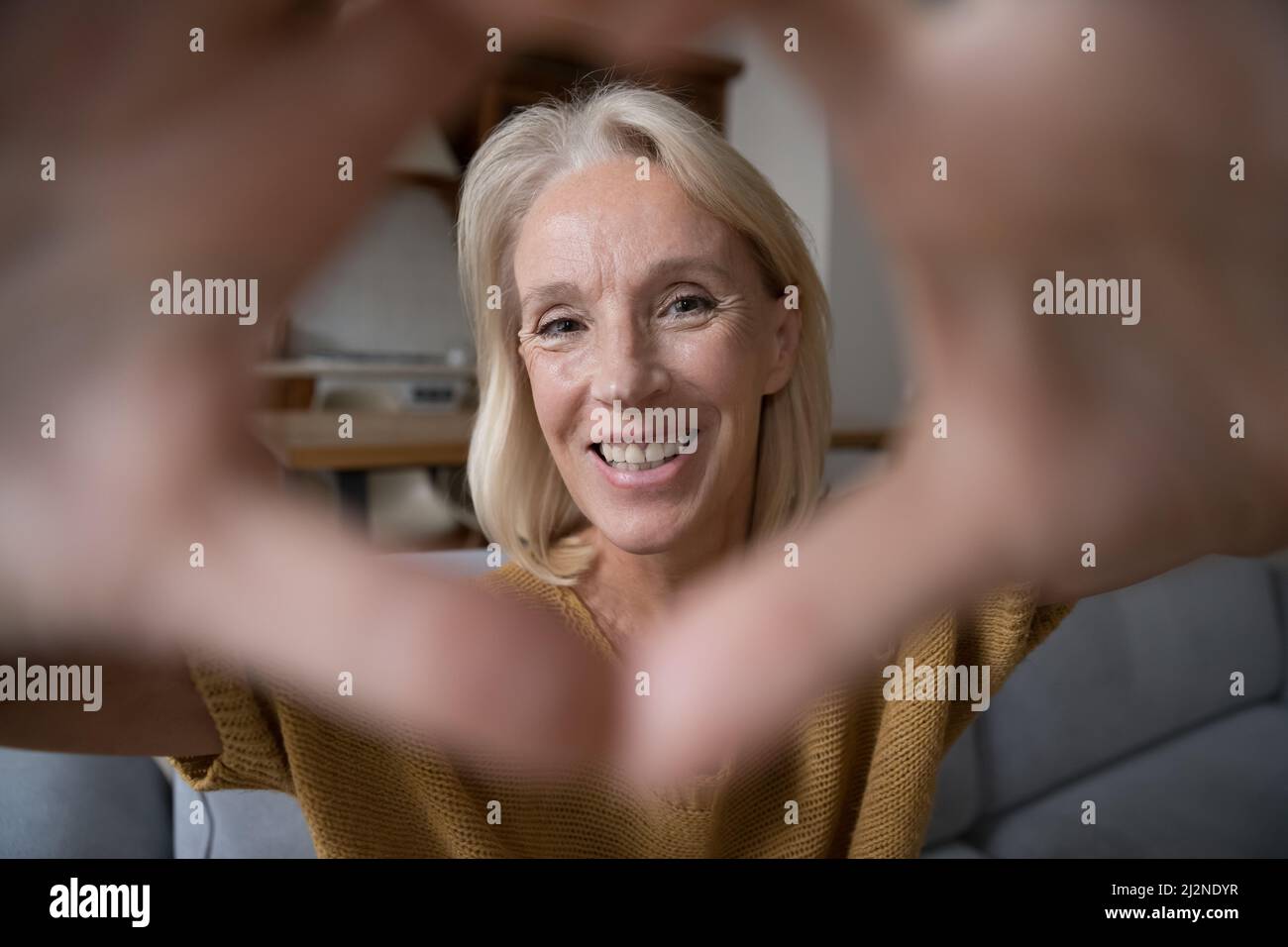Fröhliche reife Frau, die durch das Herz des Handfingers auf die Kamera schaut Stockfoto
