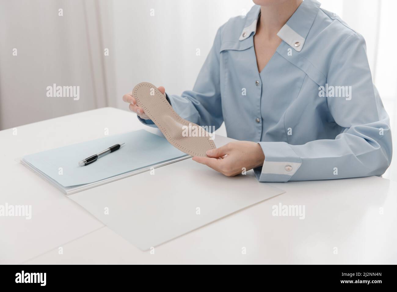 Arzt, der eine Einlegesohle hält, während er an einem Tisch sitzt. Orthopäde testet das medizinische Gerät. Orthopädische Einlagen. Fußpflege. Korrektur Der Flachen Füße Stockfoto