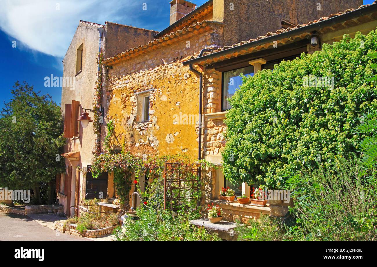 Blick auf ockerfarbenen Naturstein-Bauernhaus im provenzalischen Stil mit üppigem grünen Garten, blauem Himmel - Roussillon, Frankreich Stockfoto