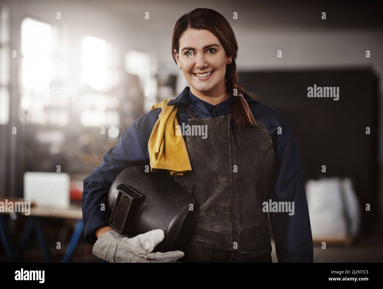 Man muss einen Helm haben. Ein Porträt einer attraktiven jungen kreativen Kunsthandwerkerin, die in ihrer Werkstatt steht und ihren Helm unter sich versteckt Stockfoto