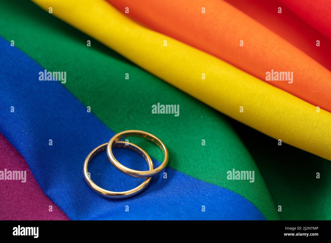 Homosexuelle Ehe mit Homosexuellen. Paar goldene Ringe auf regenbogenfarbenem Textil mit Falten, Nahaufnahme. Speicherplatz kopieren. Stockfoto