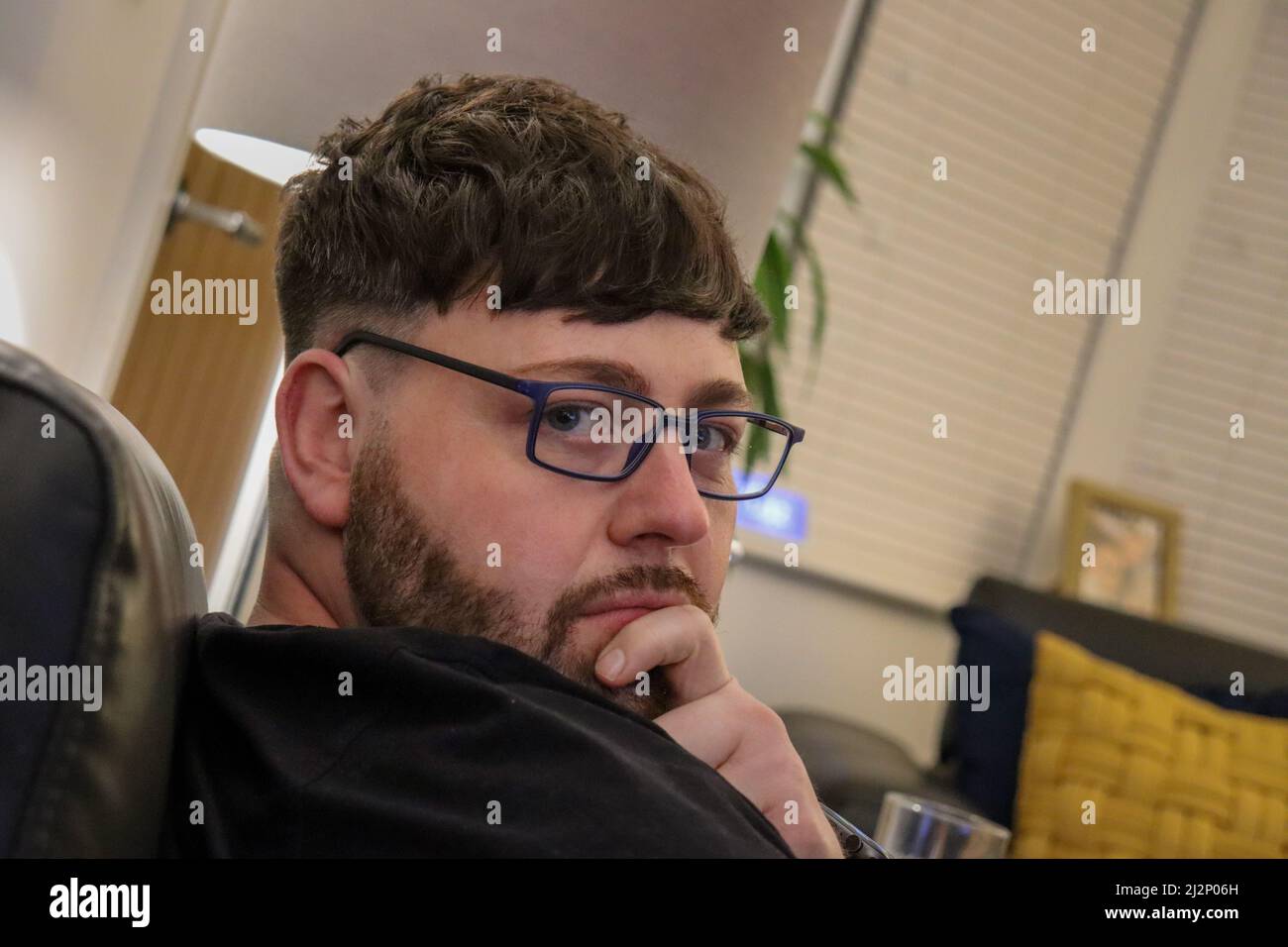 Junger Mann mit fabelhaften Haaren, der mit einer Brille über die Schulter schaut Stockfoto