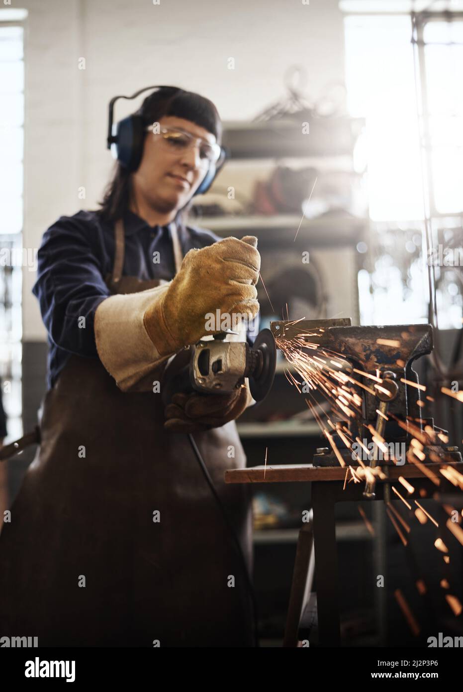 Zermahlen. Ausgeschnittene Aufnahme einer attraktiven jungen Kunsthandwerkerin mit einem Winkelschleifer in ihrer Werkstatt. Stockfoto