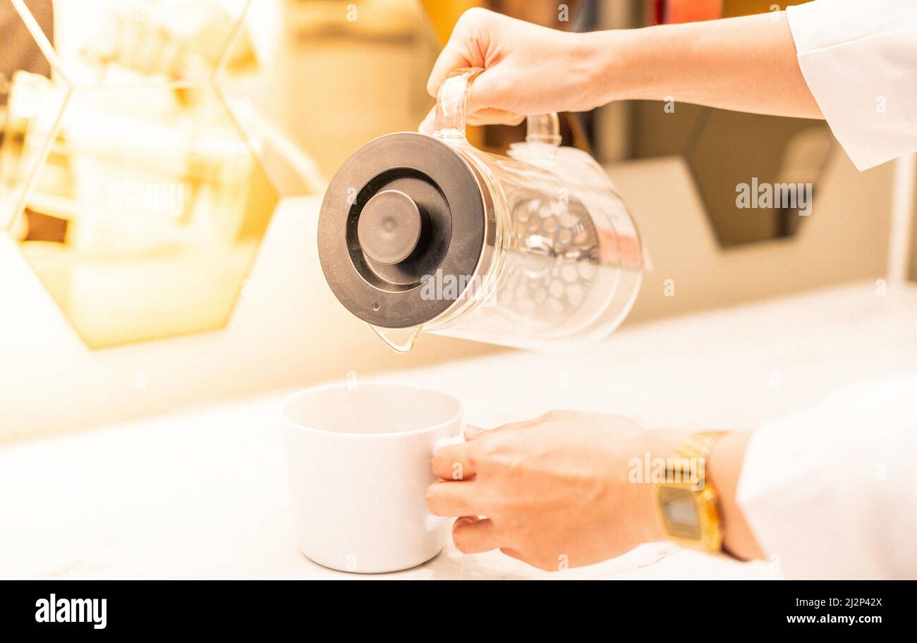 Hand hält einen weißen Becher und bereitet das Wasser mit dem weißen Hintergrund vor. Stockfoto