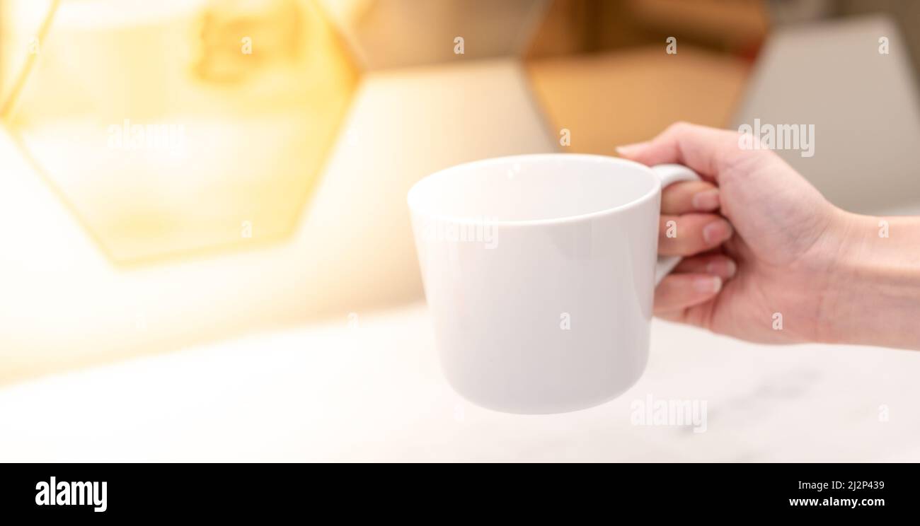 Hand hält einen weißen Becher und bereitet das Wasser mit dem weißen Hintergrund vor. Stockfoto