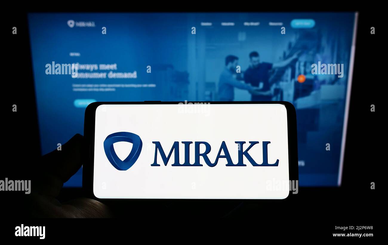 Person, die ein Mobiltelefon mit dem Logo des französischen E-Commerce-Softwareunternehmens Mirakl auf dem Bildschirm vor der Business-Webseite hält. Konzentrieren Sie sich auf die Telefonanzeige. Stockfoto