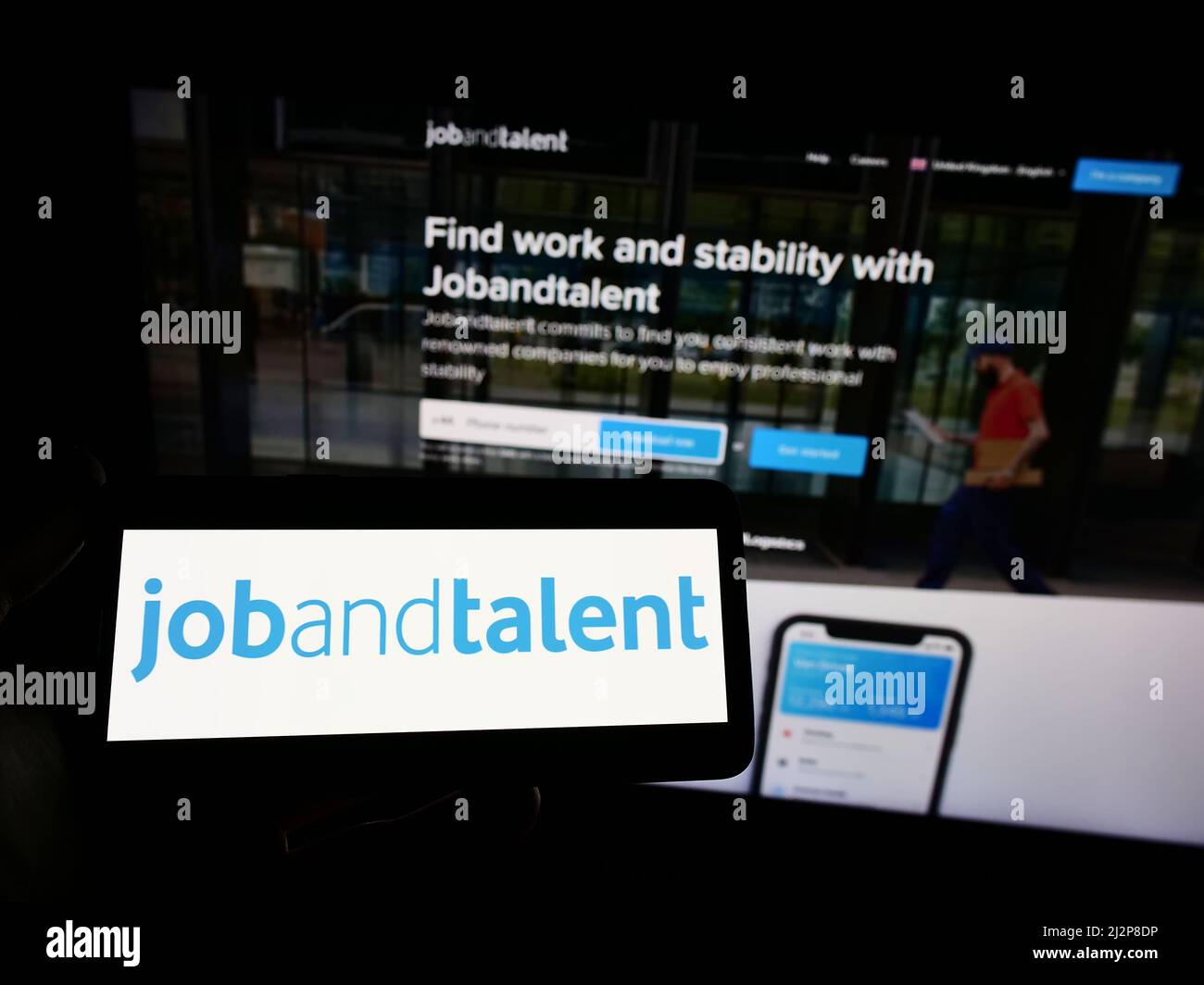 Person, die das Smartphone mit dem Logo der Firma Jobs and Talent S.L. (Jobandtalent) auf dem Bildschirm vor der Website hält. Konzentrieren Sie sich auf die Telefonanzeige. Stockfoto