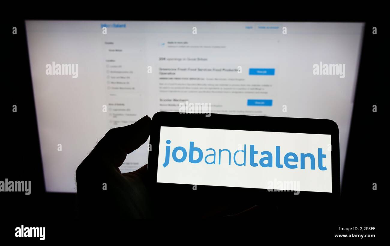 Person mit Mobiltelefon und Logo der Firma Jobs und Talent S.L. (Jobandtalent) auf dem Bildschirm vor der Webseite. Konzentrieren Sie sich auf die Telefonanzeige. Stockfoto