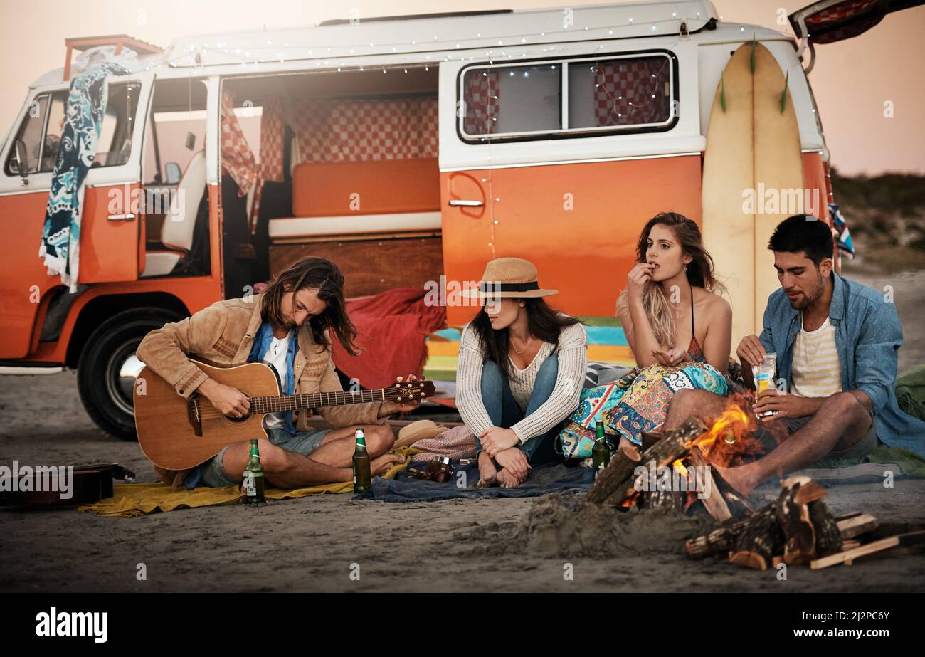 Wir kommen zusammen und Viel Spaß. Aufnahme einer Gruppe von Freunden, die am Strand um ein Feuer herum sitzen. Stockfoto