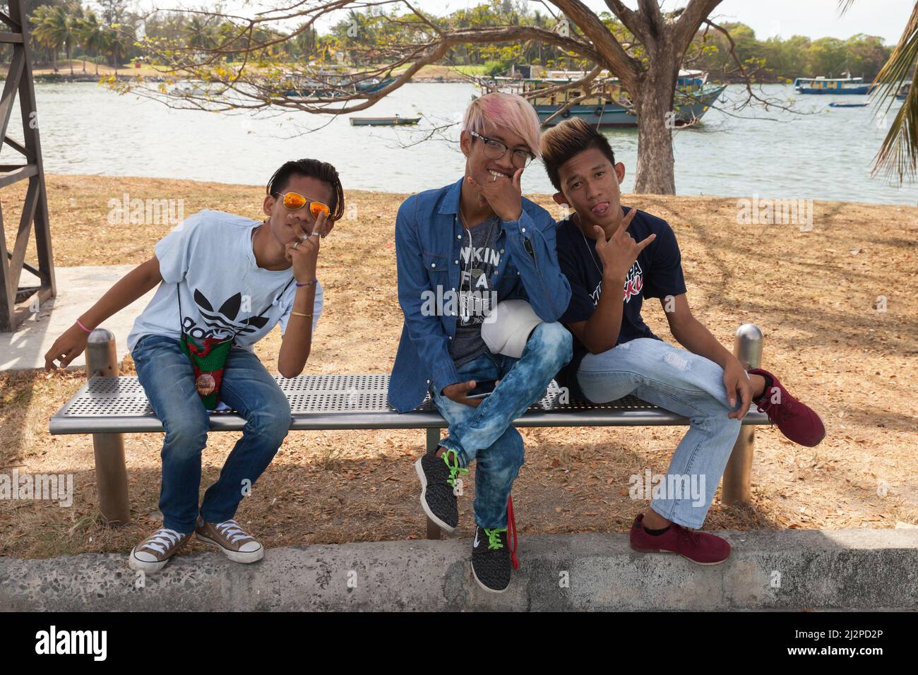 Kota Kinabalu, Malaysia - 17. März 2019: Porträt von drei positiven malaysischen Jungen, die auf einer Bank im öffentlichen Park von Kota Kinabalu sitzen Stockfoto