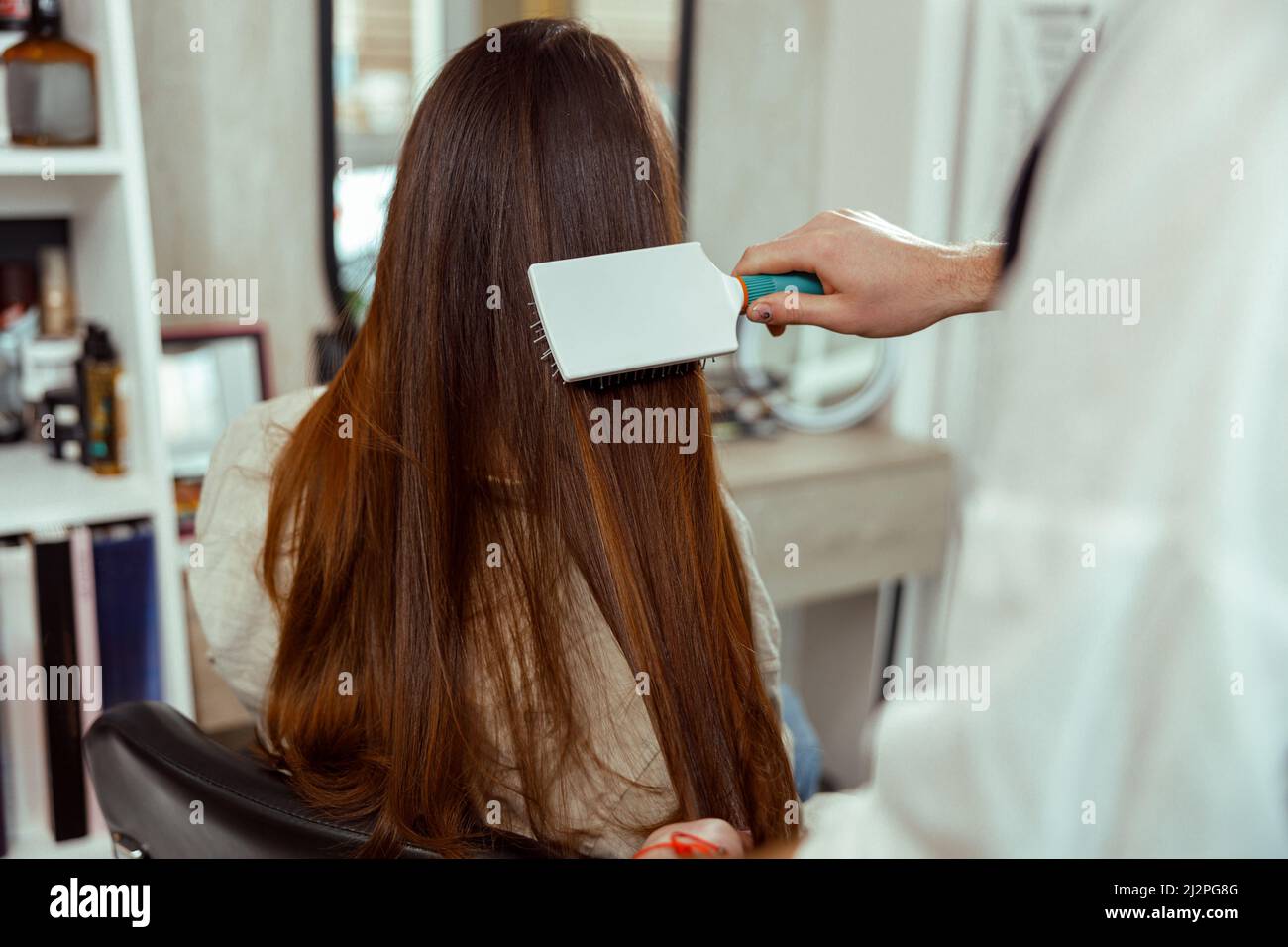 Hand des Friseurs bürstet lange und glänzend braune Haare der jungen Frau im Schönheitssalon Stockfoto