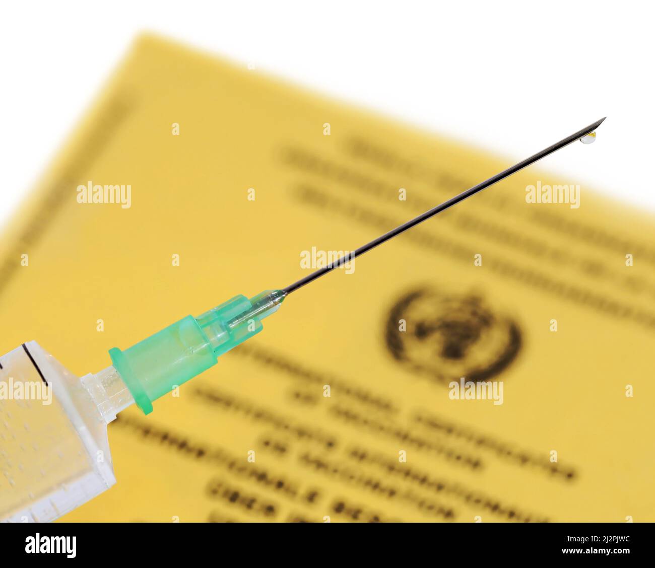 Medizinische Spritze gefüllt mit Impfstoff und gelbem internationalen Impfzertifikat auf weißem Hintergrund, Nahaufnahme einer Impfnadel Stockfoto