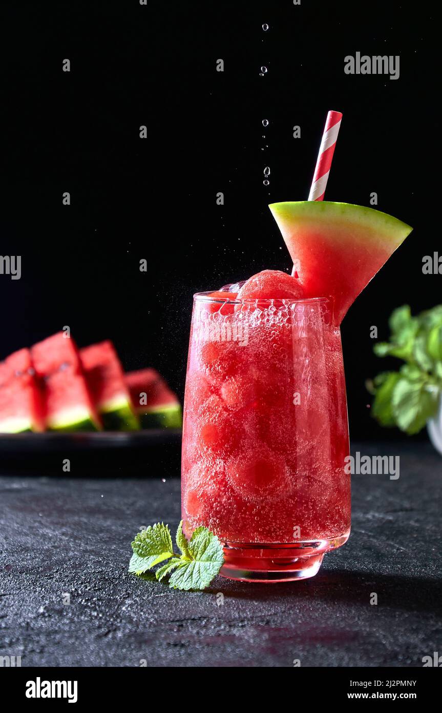Reife Wassermelonen-Noisette-Kugeln mit sada im Glas und fallenden Wassertropfen auf dunklem Hintergrund. Erfrischender Sommerdrink Stockfoto