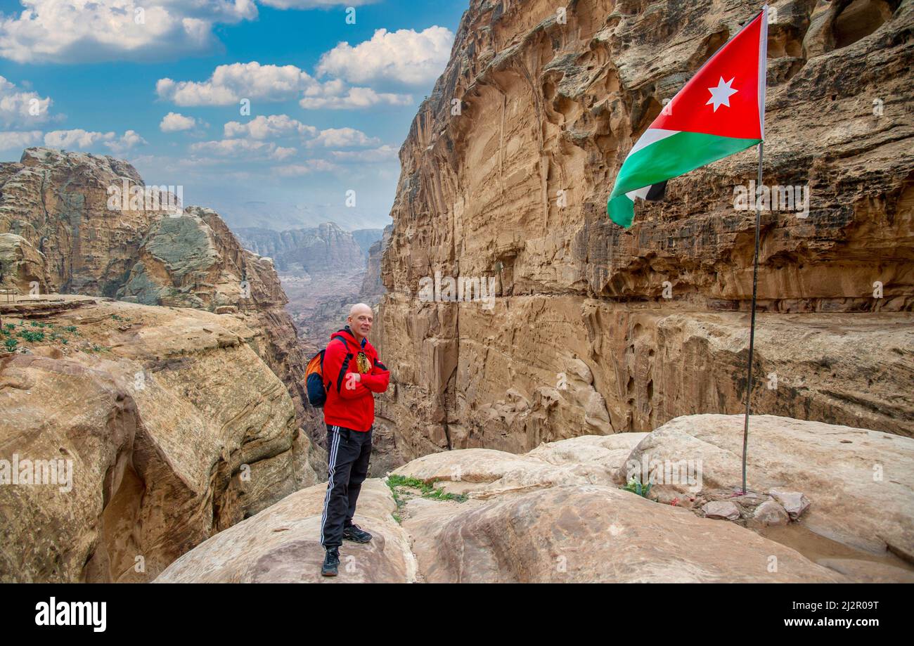 Ein Tourist posiert neben der jordanischen Flagge, die in Petra fliegt, mit schönen roten Bergen im Hintergrund und blauem Himmel 20. Februar 2020 Stockfoto