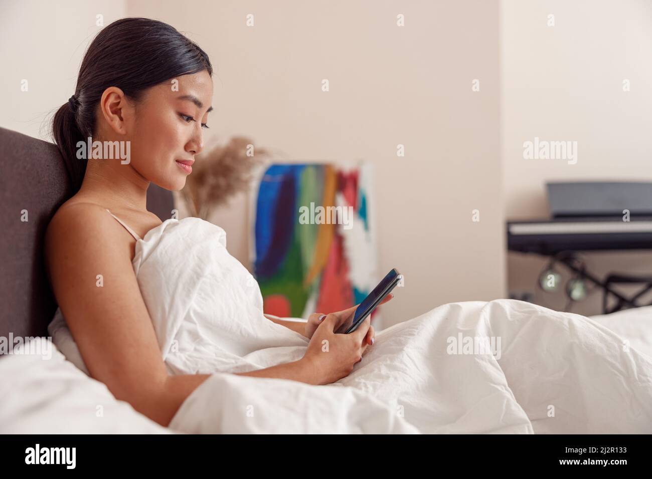 Asiatische junge Frau mit Mobiltelefon zu Hause Stockfoto