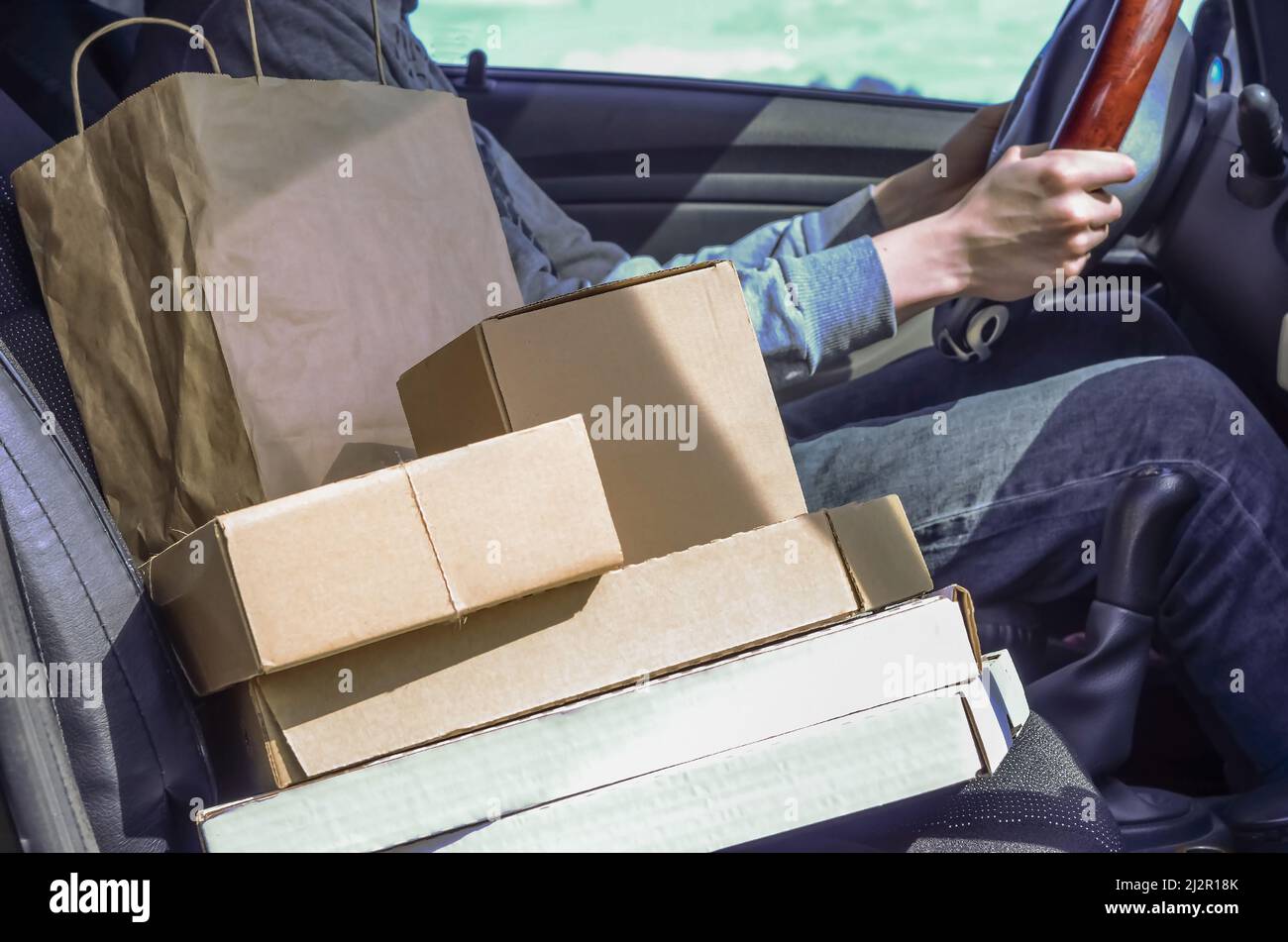 Kurier mit Paketen im Auto. Lieferung von Paketen, Waren, Pizza. Lieferer. Sichere Lieferung während der Quarantäne des Coronavirus. Stockfoto