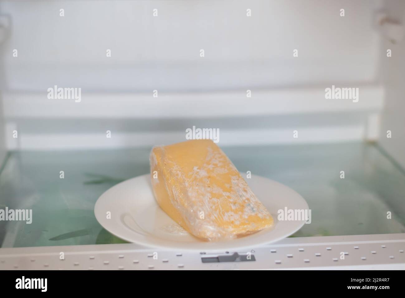 Schimmeliger Käse, eingewickelt in Frischhaltefolie im Kühlschrank. Falsche Lagerung, verdorbenes Produkt, abgelaufenes Konzept. Stockfoto