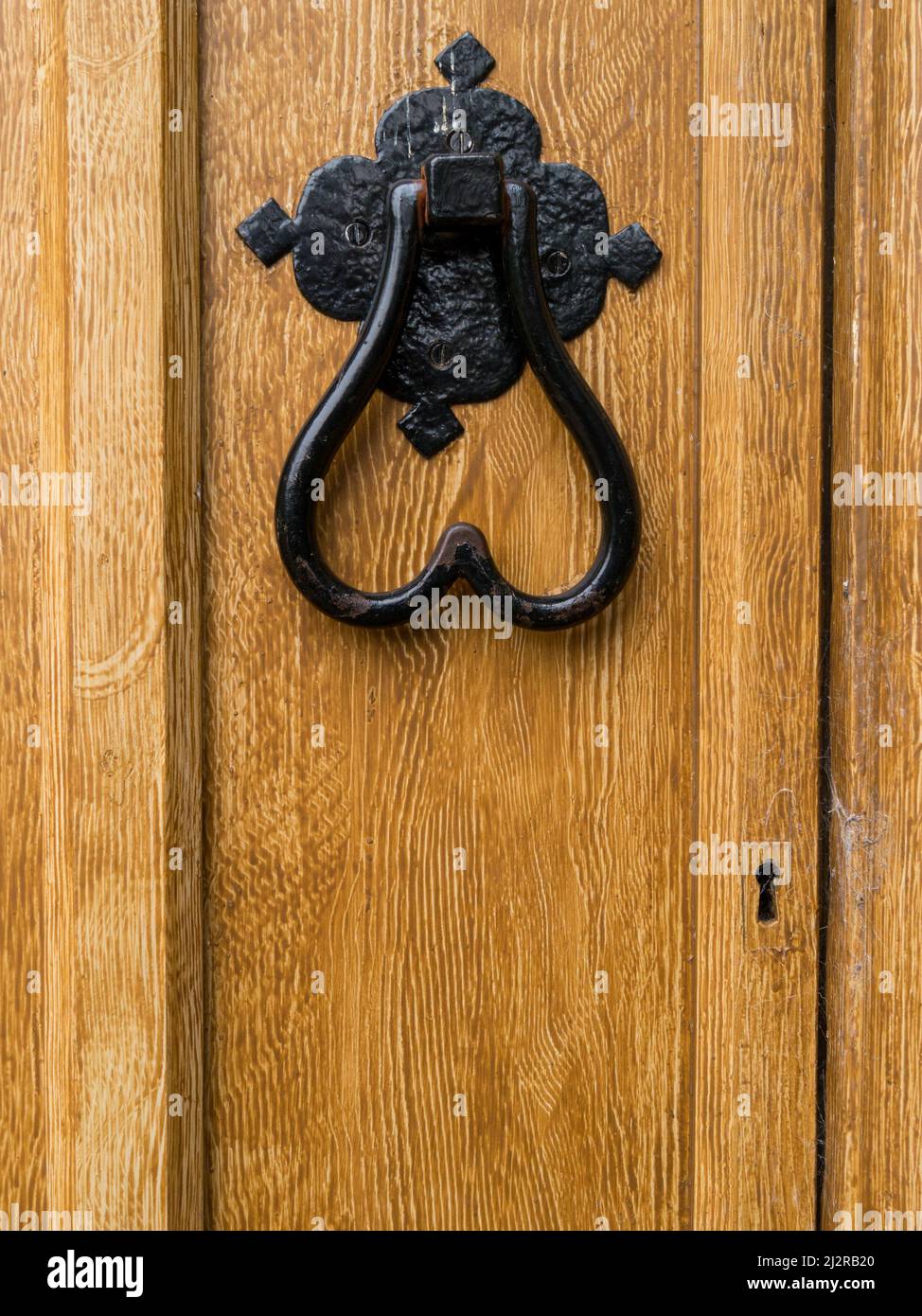 Schwarz bemalter herzförmiger schmiedeeiserner Türklopfer auf Holztür, lackiert mit hellbraunem Fake-Wood-Grain-Effekt. Stockfoto