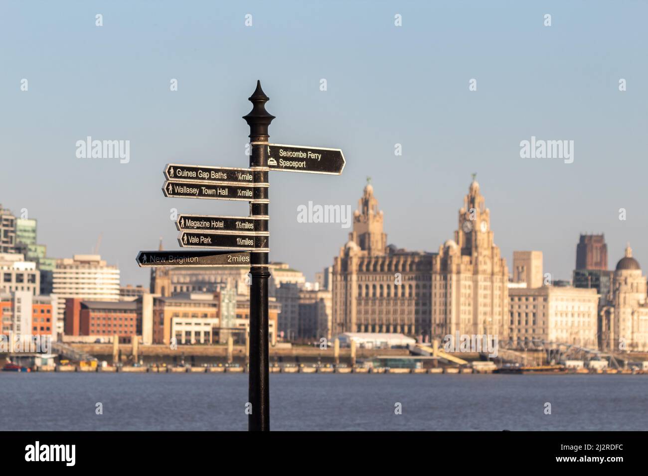 Seacombe, Großbritannien: Fingerpost-Schild an der Wallasey-Promenade mit dem Fluss Mersey und Gebäuden am Wasser im Hintergrund. Stockfoto