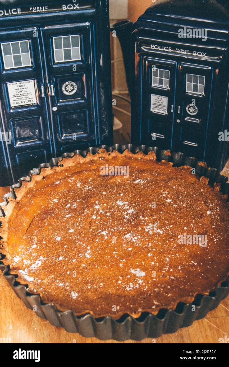 Doctor Who Tardis Memorabilia steht neben einem frisch gebackenen Kürbiskuchen, der mit weißem Zucker bestreut ist. Stockfoto