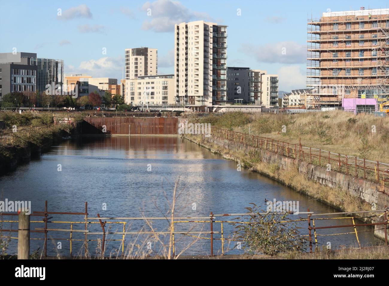 Stillgelegtes Graving Dock Becken wartet auf Neubau, Cardiff Bay Wales, Großbritannien. Gehäuseblöcke im Hintergrund Stockfoto