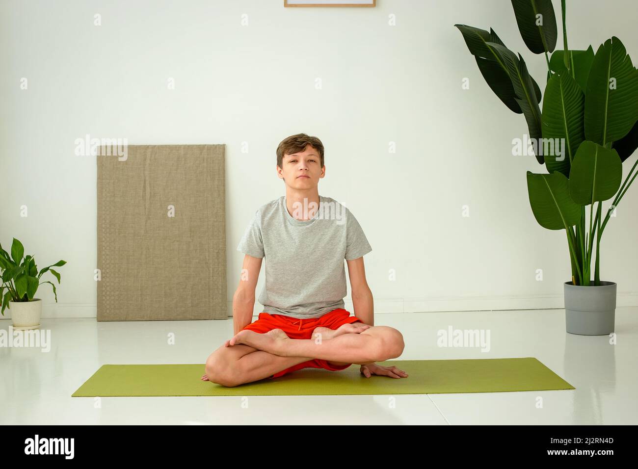 Ein Teenager sitzt in der Lotusposition in einem hellen Raum Stockfoto