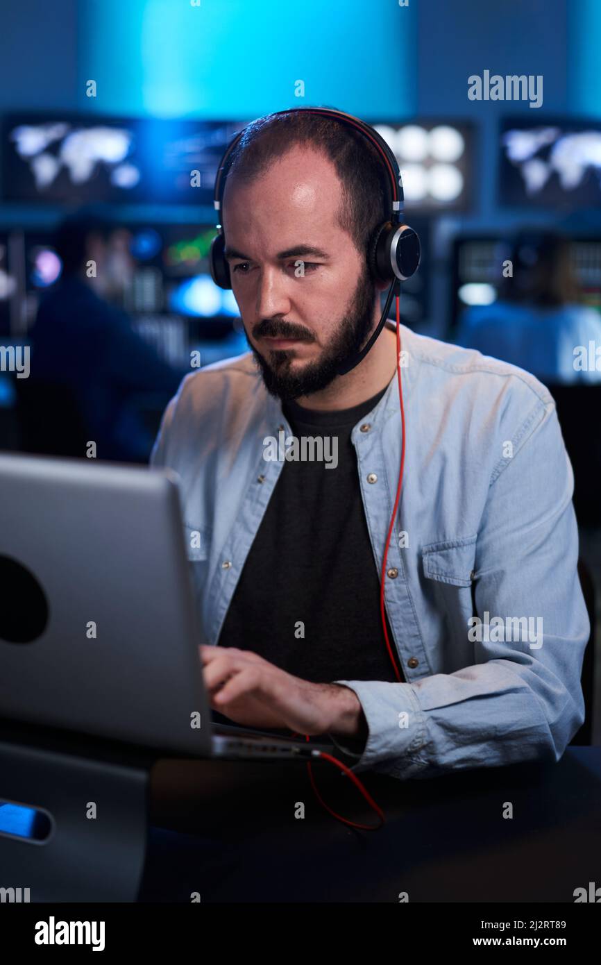 Vertikales Foto eines Börsenmaklers, der in einem dunklen Büro mit Bildschirmen ein Gespräch führt. Professioneller IT-Techniker, der am Computer arbeitet Stockfoto