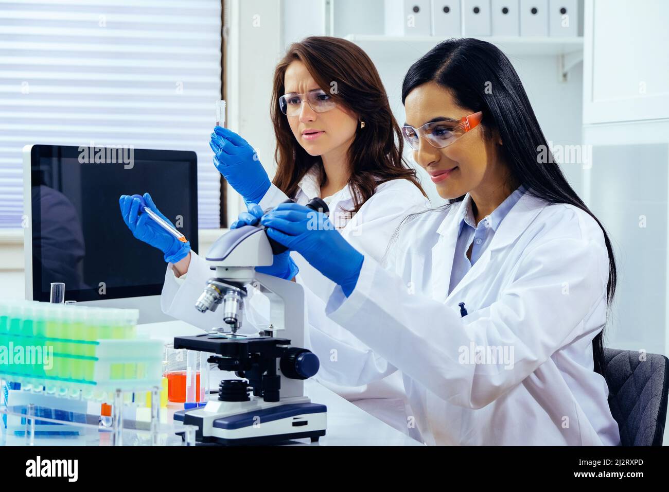 Zwei schöne junge Wissenschaftlerinnen, die im Labor mit Reagenzgläsern und Mikroskop arbeiten, um in der pharmazeutischen Industrie zu forschen Stockfoto
