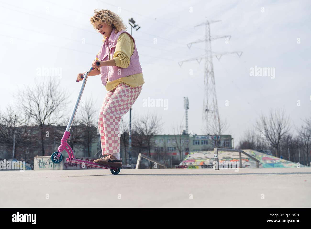 Aufgeregt junge blonde Hipster Frau fährt einen rosa Roller auf dem Sportplatz Kopie Raum voller Schuss . Hochwertige Fotos Stockfoto