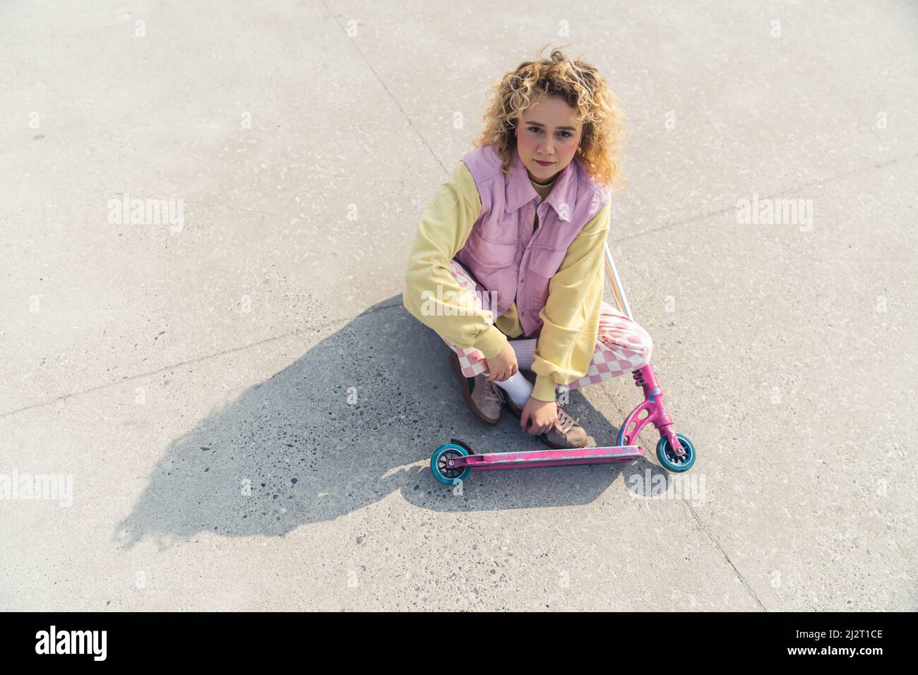 Die hübsche junge, frisch gesichtige blonde Frau sitzt auf dem rosafarbenen Roller vor ihrem Blick auf die Kamera voller Schuss-Kopierraum. Hochwertige Fotos Stockfoto