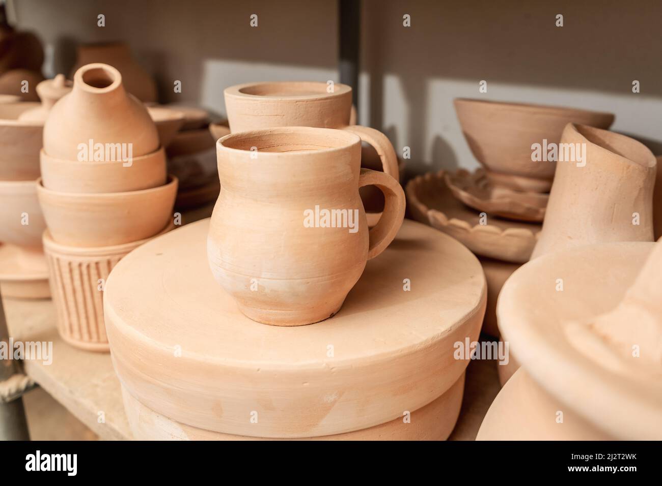 Regale mit Schüsseln, Tellern, Gläsern, Teekannen usw. aus Ton in natürlicher Rohfarbe bis zum endgültigen Gemälde. Kunsthandwerk aus Lehm. Stockfoto