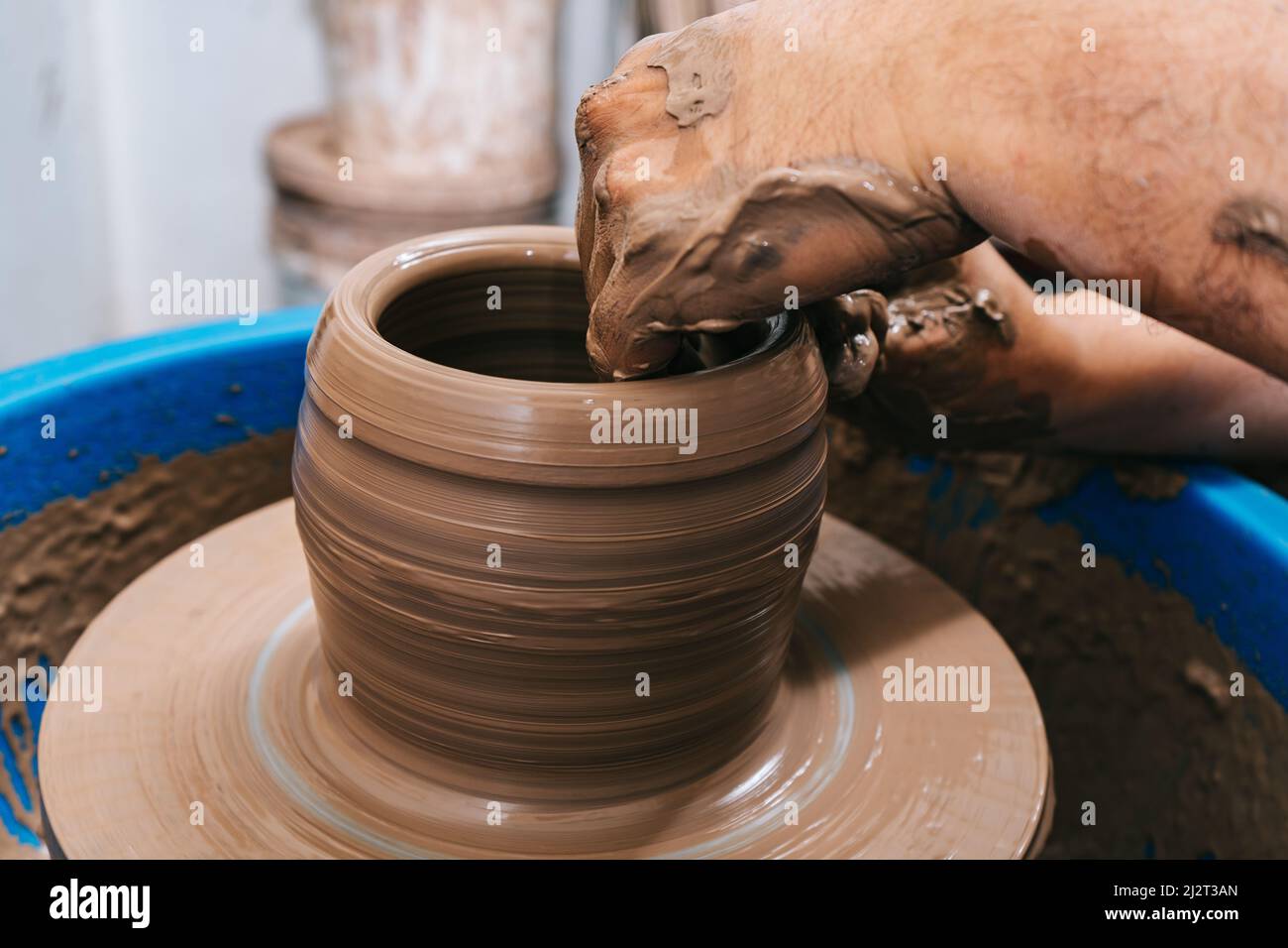 Die erfahrenen Hände eines Töpfers, der Ton auf einem Töpferrad arbeitet. Der Ton nimmt die Form an, die der Töpfer ihm mit dem Terrakotta-Ton des Tones gibt. Stockfoto