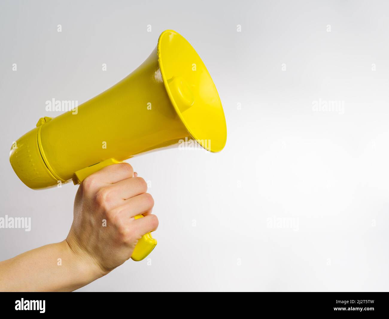 Gelbes Megaphon in der Hand eines Mannes auf weißem Hintergrund. Minimalismus. Es ist freier Speicherplatz zum Einfügen vorhanden. Symbol für falsche Informationen, Gerüchte, Fälschungen. Journal Stockfoto