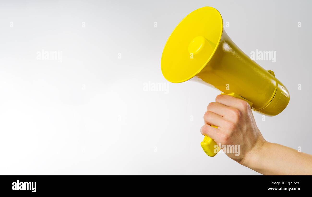 Die Hand eines Mannes hält ein gelbes Megaphon auf weißem Hintergrund. Es symbolisiert Gerüchte, Fälschungen, falsche Informationen. Wahlen, Debatten, Journalismus, Werbung Stockfoto