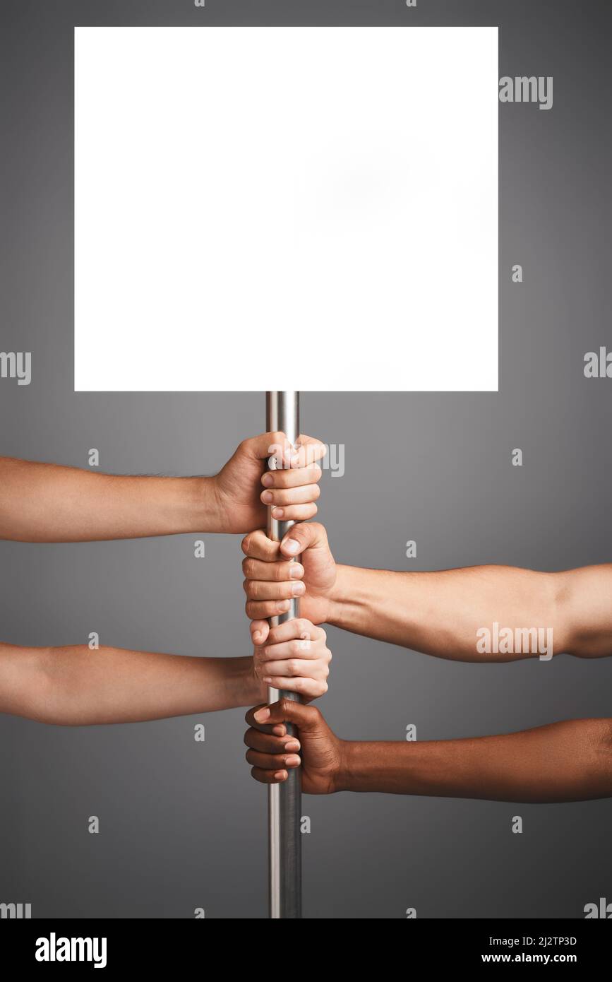 Nun, bringen Sie unseren Punkt rüber. Studioaufnahme von nicht identifizierbaren Händen, die sich vor grauem Hintergrund an einem Poster festhalten. Stockfoto