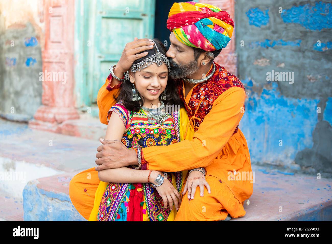 Traidtional indischer Vater küsst auf die Stirn seiner culte kleine Tochter in bunten Outfits, Mann trägt Turban und Mädchen tragen Schmuck. Parentho Stockfoto