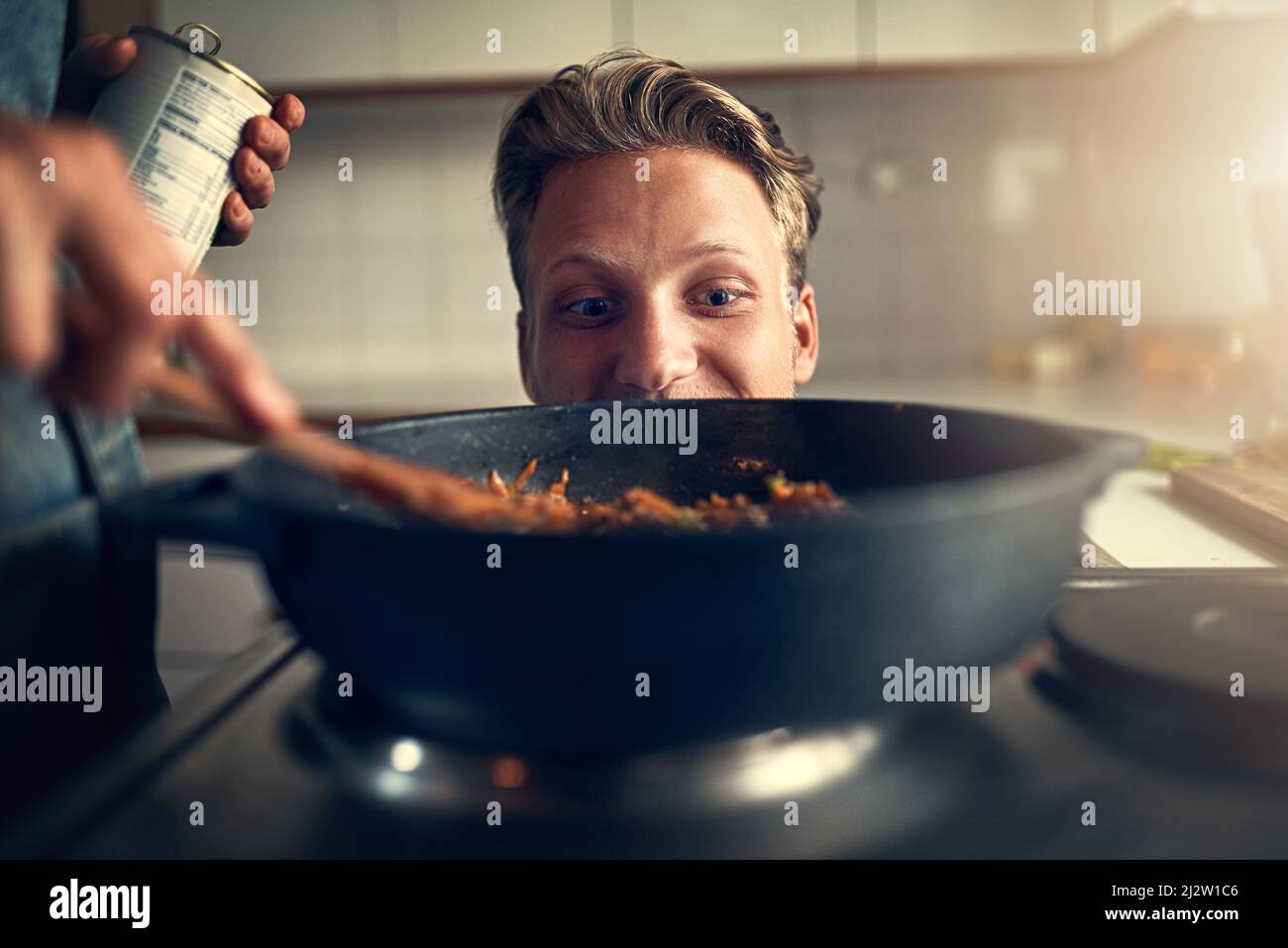 Etwas riecht gut. Aufnahme eines jungen Mannes, der seine Mutter beim Kochen auf dem Herd in ihrer Küche zu Hause beobachtete. Stockfoto