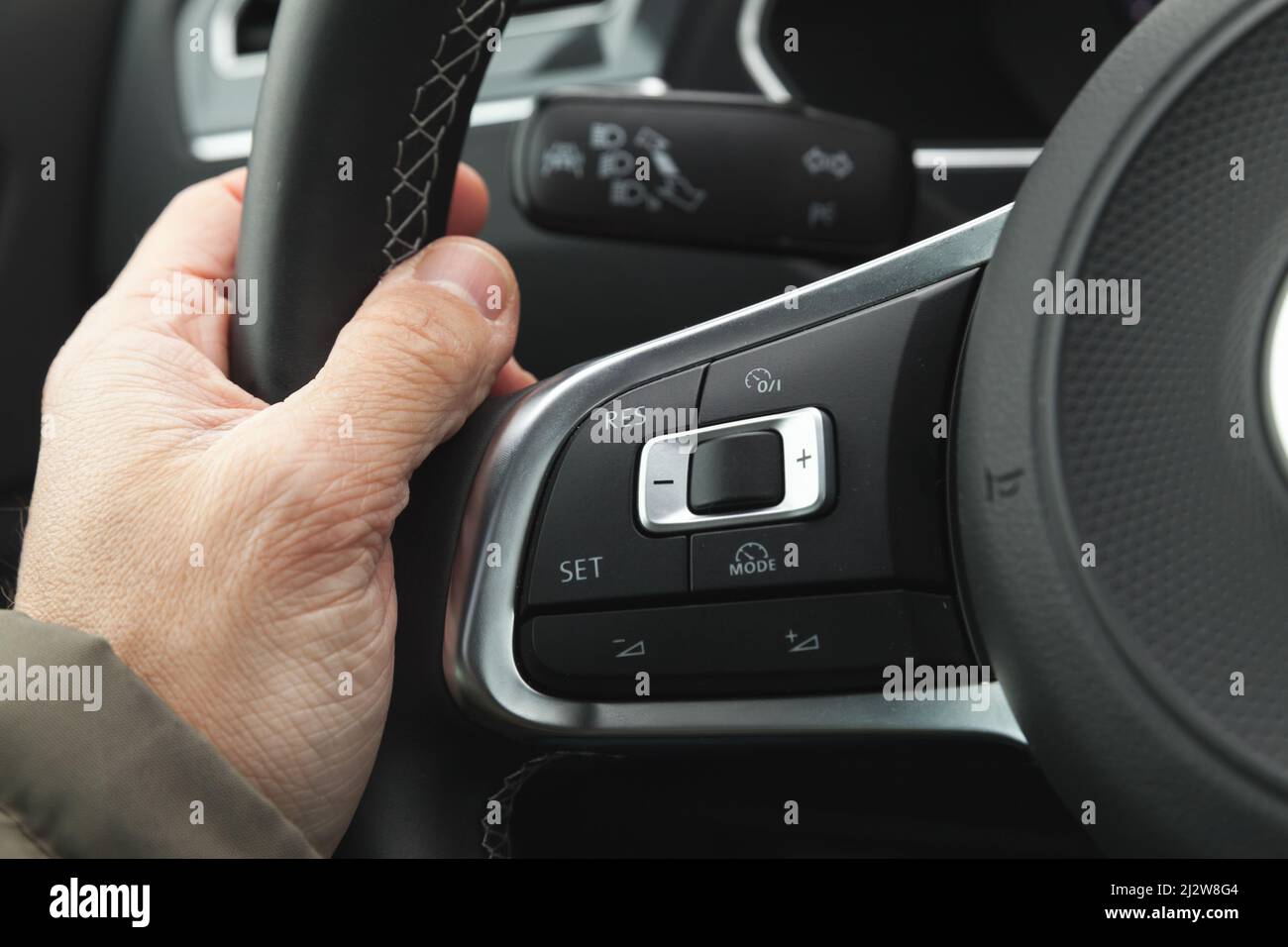 Tempomat- und Lautstärketasten am modernen Lenkrad des Autos, Innenraumdetails mit Fahrerhand Stockfoto